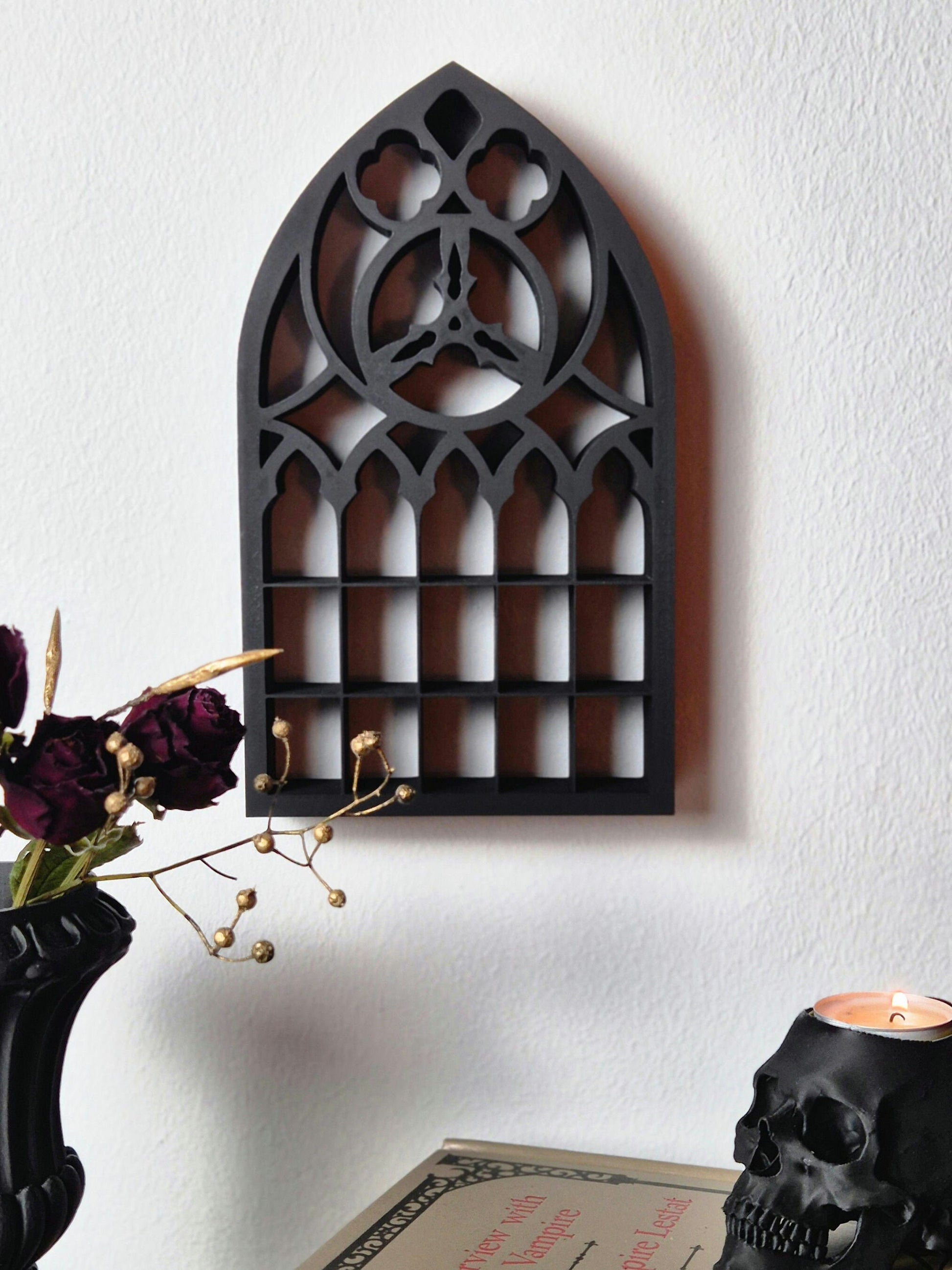 May include: Black wooden gothic window frame wall decor with a pointed arch and intricate details. The frame is mounted on a white wall.