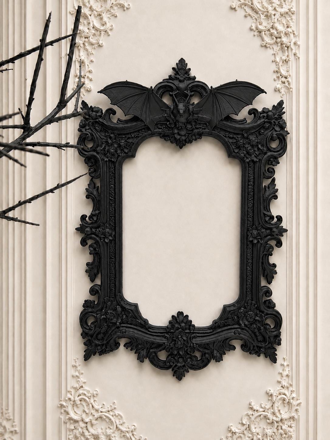 May include: Ornate black picture frame with a bat motif at the top. The frame has a detailed, gothic design with floral and scrollwork accents. The frame is mounted on a cream-colored wall with decorative molding.